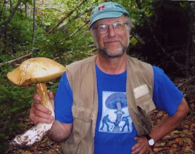 Lawrence Millman in a forest, holding a large bolete.