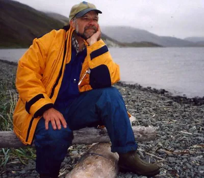 Lawrence Millman in a yellow jacket on a gravel beach in Siberia.